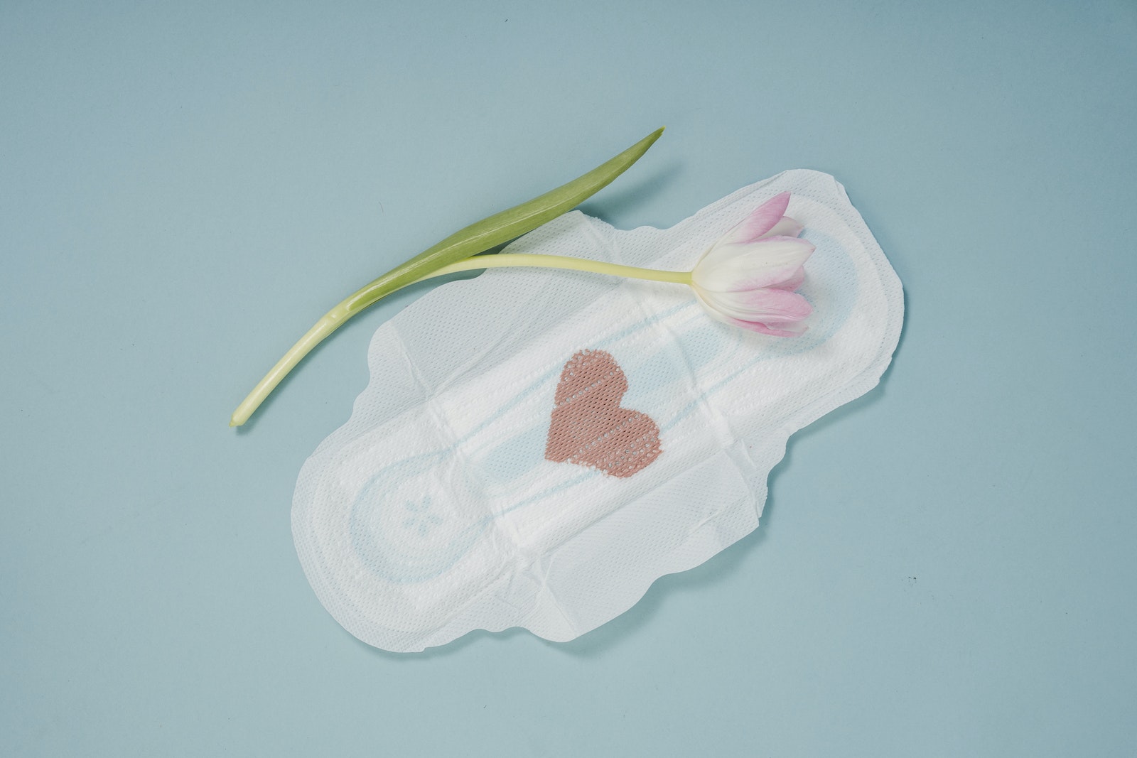 Feminine hygiene pad and pink tulip placed on blue background